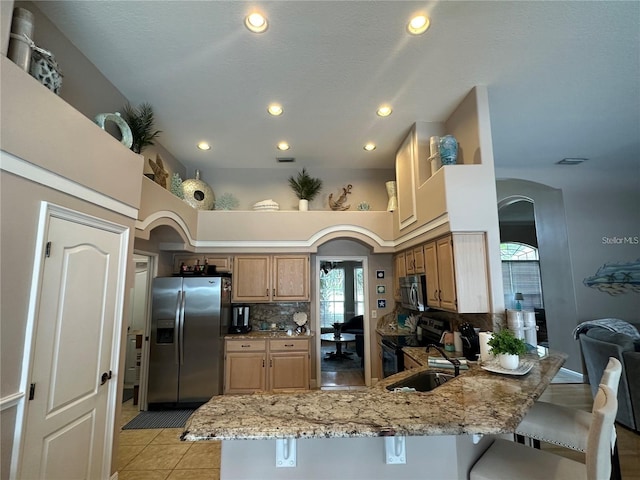 kitchen featuring kitchen peninsula, stainless steel appliances, light stone countertops, backsplash, and a breakfast bar area