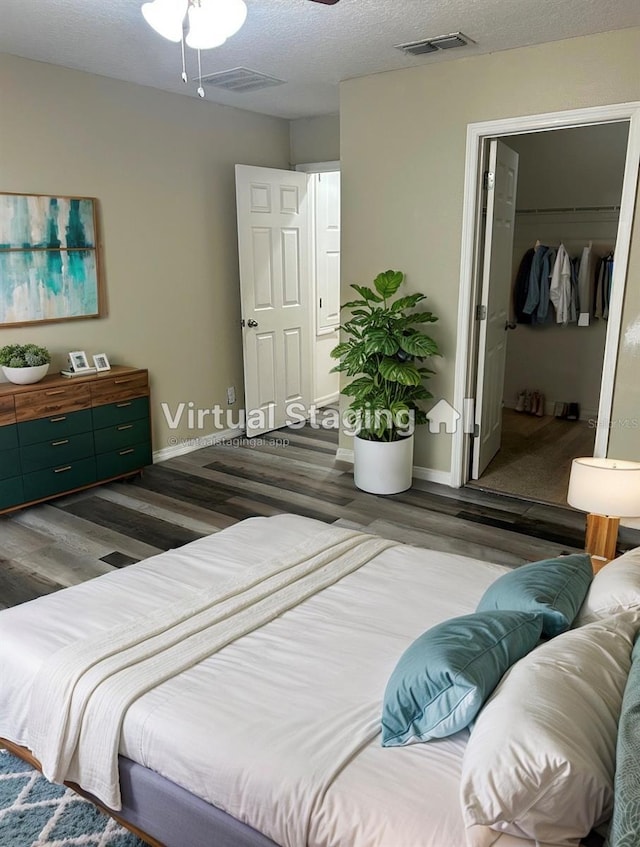 bedroom featuring dark wood finished floors, visible vents, a walk in closet, and a textured ceiling