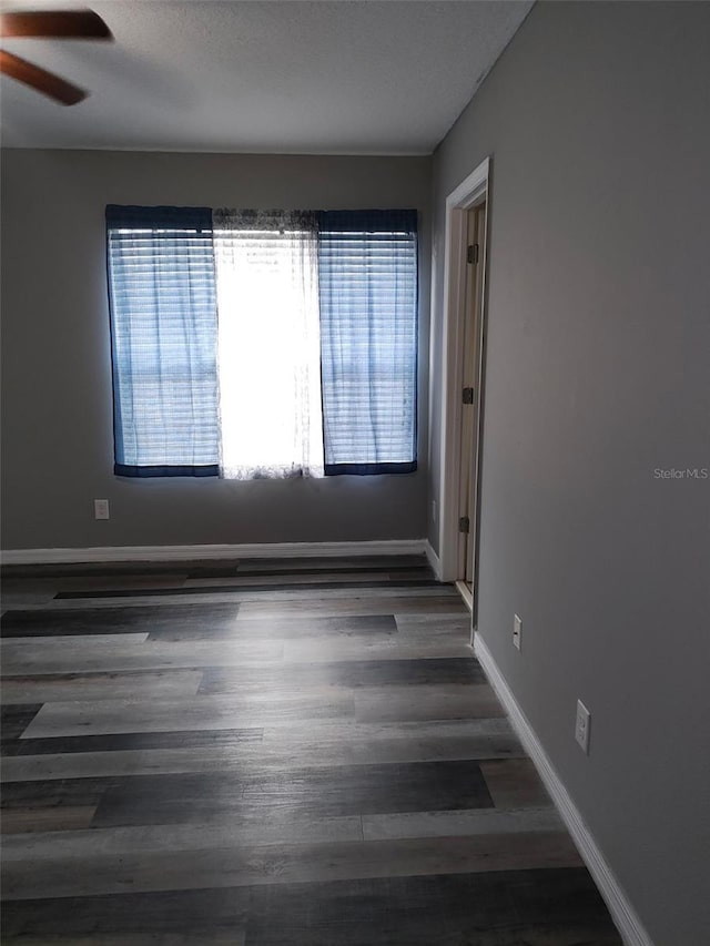 unfurnished room featuring dark wood finished floors, baseboards, and ceiling fan
