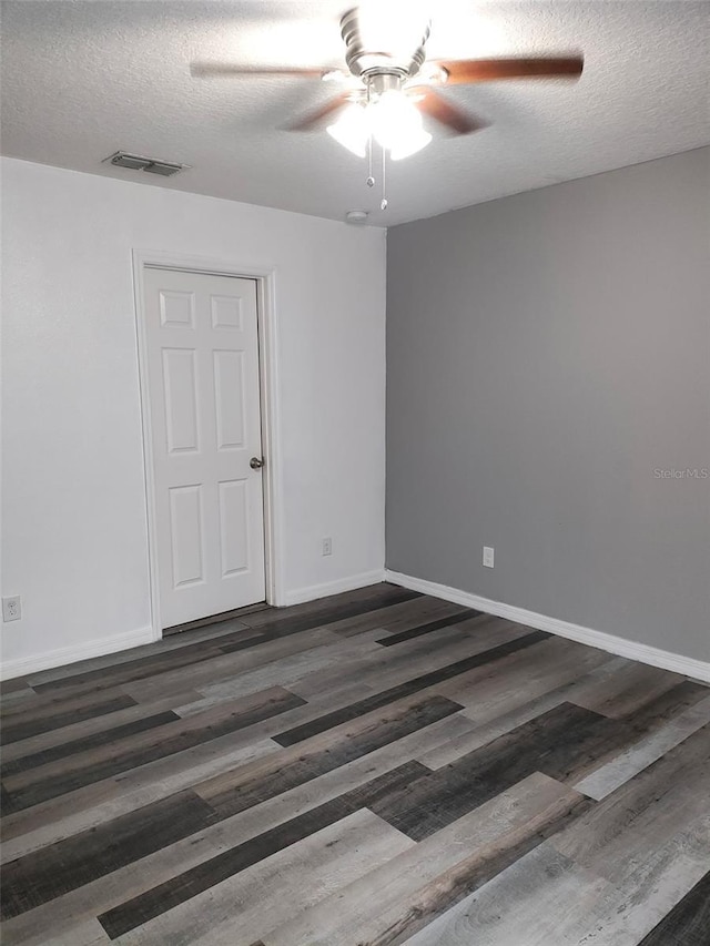 empty room featuring baseboards, visible vents, a ceiling fan, dark wood-type flooring, and a textured ceiling