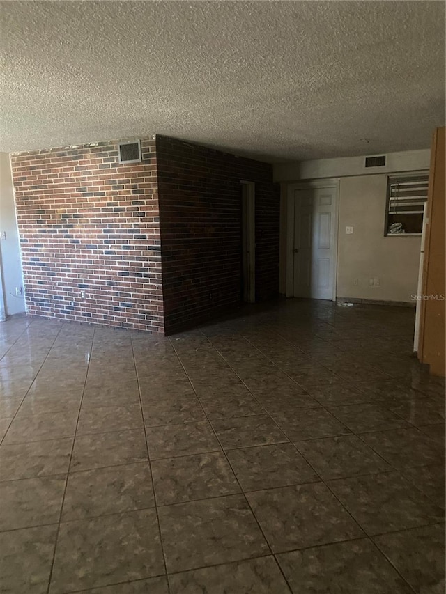 tiled empty room featuring a textured ceiling and brick wall