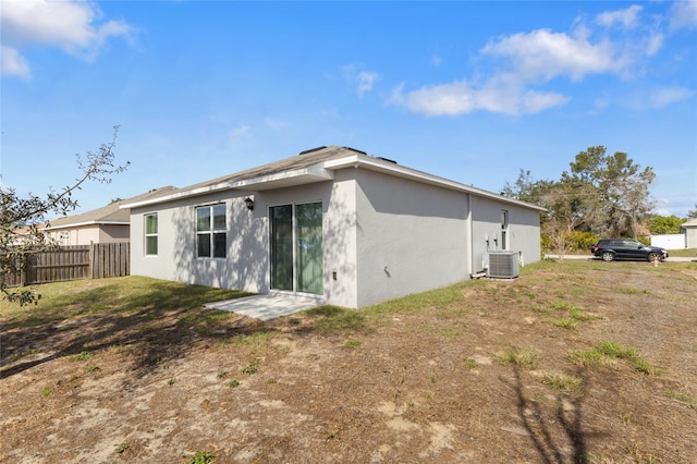 back of house featuring central AC, a lawn, fence, and stucco siding
