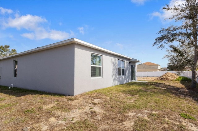 rear view of house with a yard, fence, and stucco siding