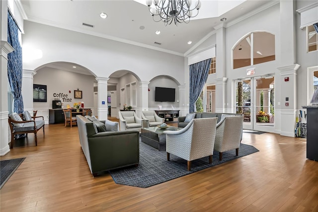 living room with a towering ceiling, light wood-style floors, visible vents, ornate columns, and crown molding