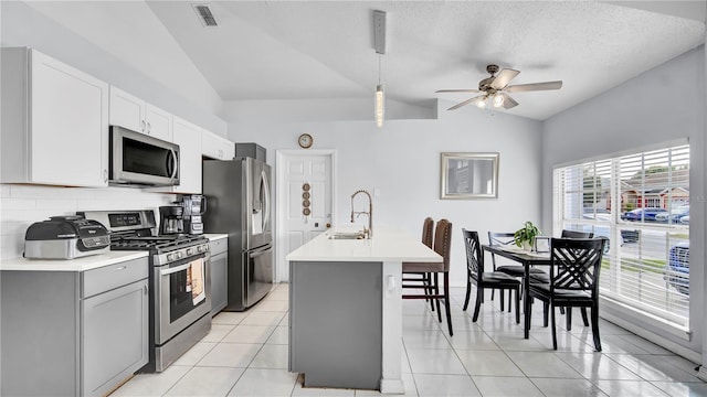 kitchen with appliances with stainless steel finishes, sink, vaulted ceiling, light tile patterned flooring, and an island with sink