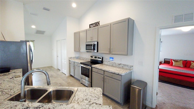 kitchen featuring vaulted ceiling, stainless steel appliances, light stone counters, and sink