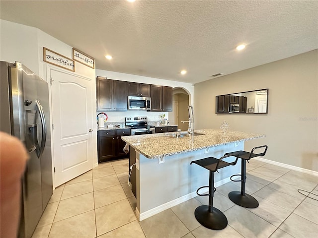 kitchen featuring dark brown cabinetry, stainless steel appliances, a breakfast bar, sink, and a kitchen island with sink