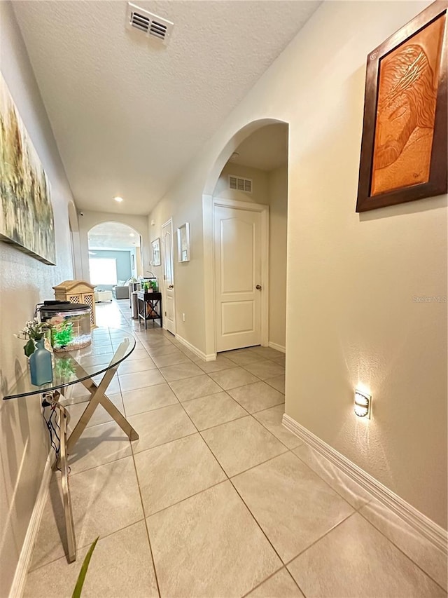 corridor with arched walkways, light tile patterned floors, and visible vents