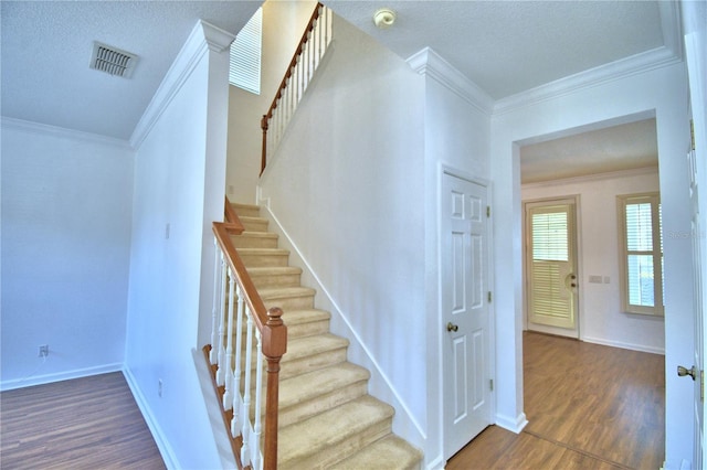 stairway featuring baseboards, visible vents, ornamental molding, wood finished floors, and a textured ceiling