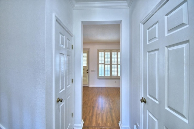 hall featuring dark wood-type flooring, crown molding, and baseboards