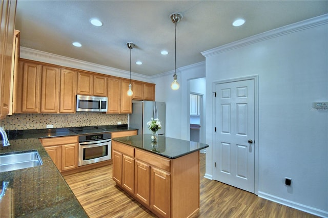 kitchen with pendant lighting, stainless steel appliances, a kitchen island, a sink, and wood finished floors