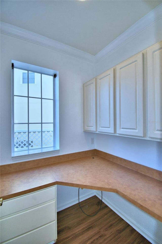 unfurnished office featuring ornamental molding, dark wood-type flooring, and built in desk