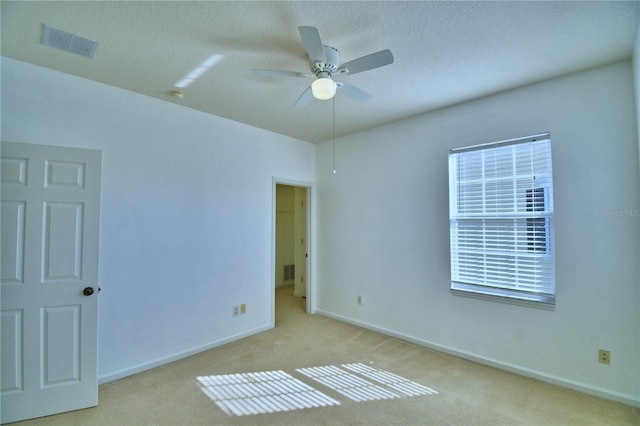 empty room featuring a textured ceiling, baseboards, visible vents, and light colored carpet