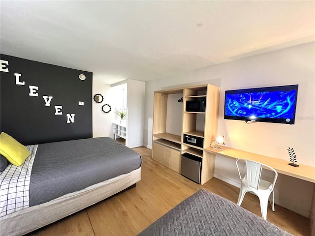 bedroom featuring built in study area, light wood-type flooring, and baseboards
