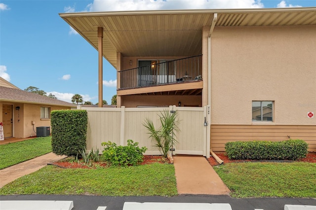 exterior space featuring stucco siding, a balcony, central AC unit, and fence