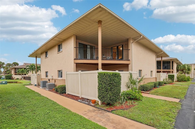 view of side of home with stucco siding, central air condition unit, fence, a yard, and a balcony