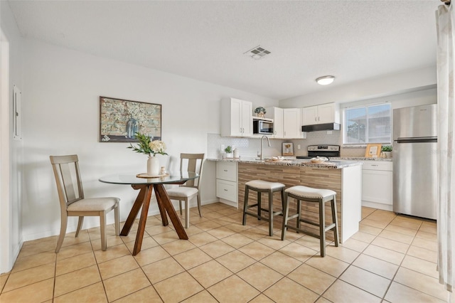 kitchen with visible vents, a sink, backsplash, stainless steel appliances, and a peninsula