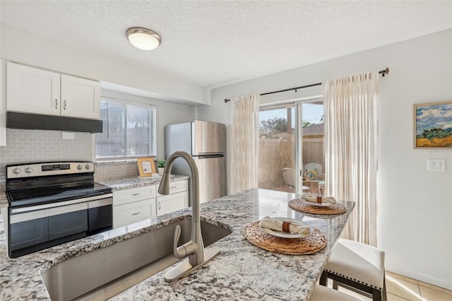 kitchen featuring light stone countertops, under cabinet range hood, decorative backsplash, a kitchen breakfast bar, and stainless steel appliances