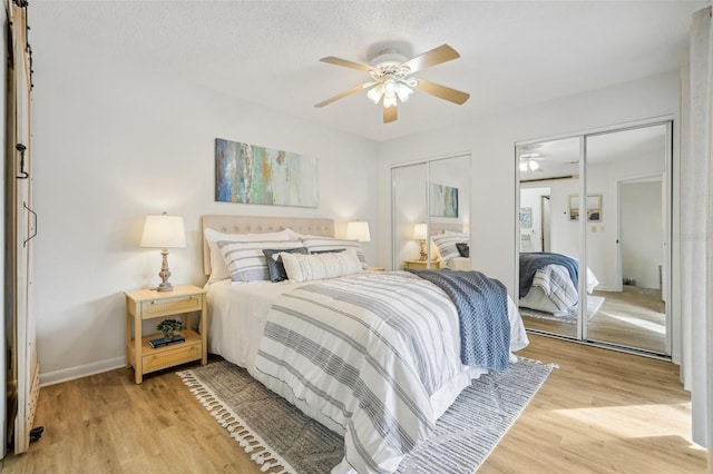 bedroom with light wood finished floors, a ceiling fan, baseboards, and two closets