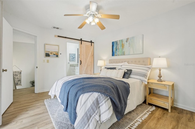 bedroom with wood finished floors, baseboards, visible vents, ceiling fan, and a barn door