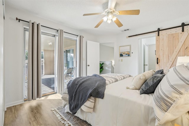 bedroom featuring wood finished floors, visible vents, a textured ceiling, a barn door, and access to outside