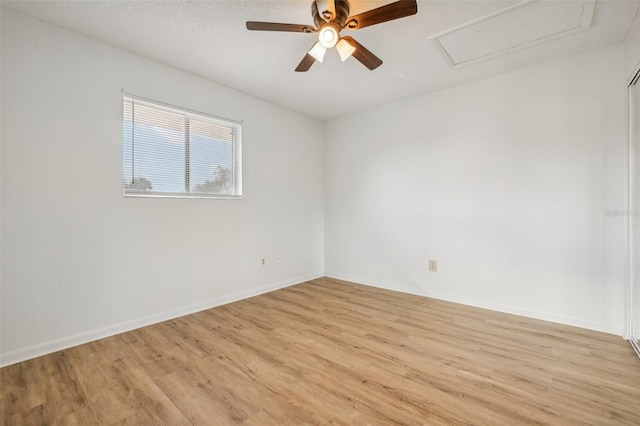 unfurnished room with ceiling fan, baseboards, attic access, and light wood-style flooring