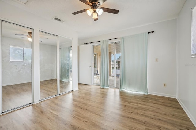 unfurnished bedroom with visible vents, two closets, wood finished floors, and a ceiling fan