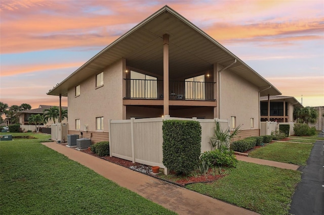 property exterior at dusk with stucco siding, a yard, central AC, and a balcony