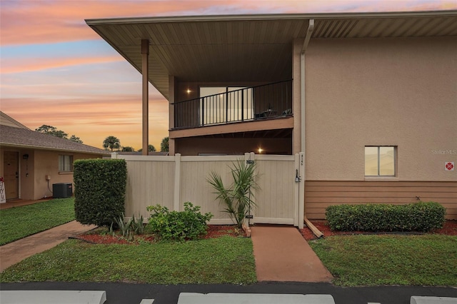 view of front of house with stucco siding, central AC, a balcony, and fence