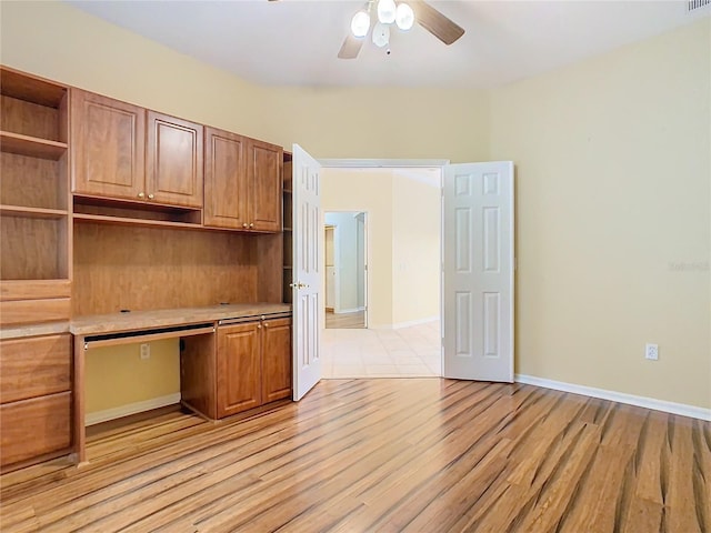 unfurnished office featuring light wood-style flooring, built in desk, baseboards, and a ceiling fan