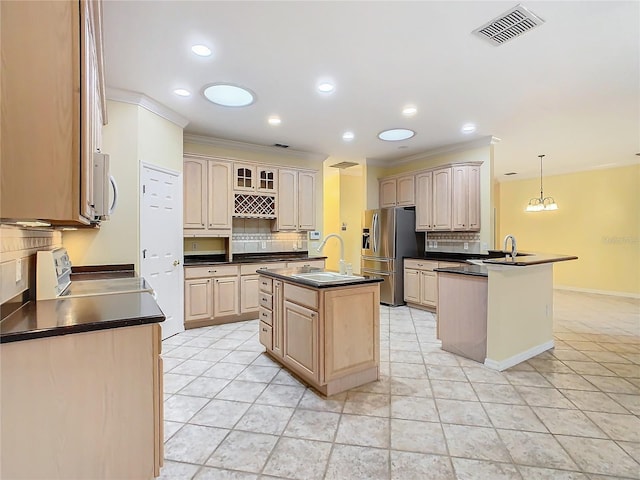 kitchen featuring visible vents, an island with sink, dark countertops, stainless steel refrigerator with ice dispenser, and a sink