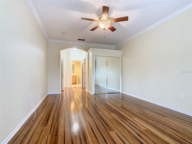 unfurnished bedroom with visible vents, arched walkways, ornamental molding, wood finished floors, and a closet