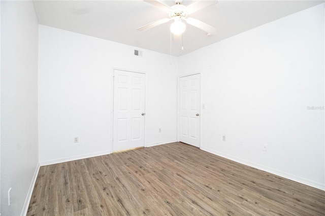 spare room with baseboards, wood finished floors, visible vents, and a ceiling fan