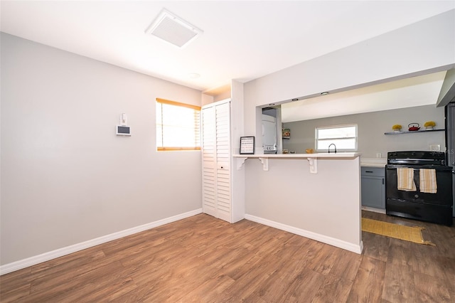 kitchen featuring a peninsula, black range with electric stovetop, a breakfast bar, visible vents, and light countertops