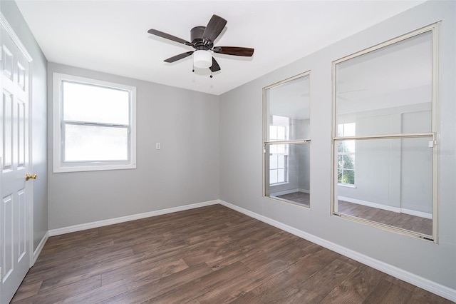 empty room with dark wood-style flooring, a ceiling fan, and baseboards