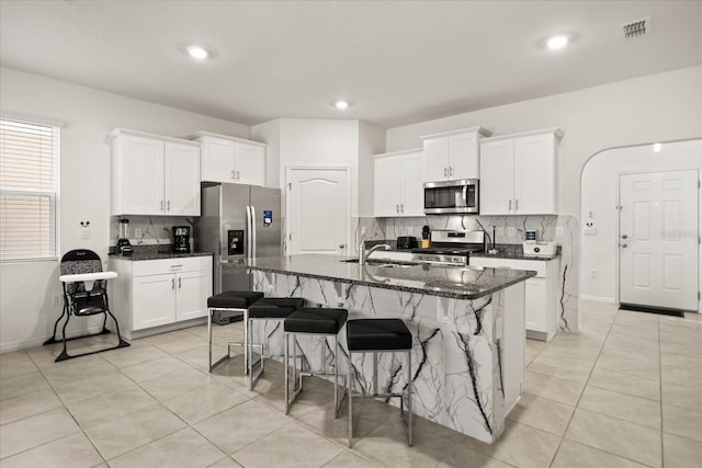 kitchen with a center island with sink, dark stone countertops, a kitchen breakfast bar, stainless steel appliances, and white cabinets