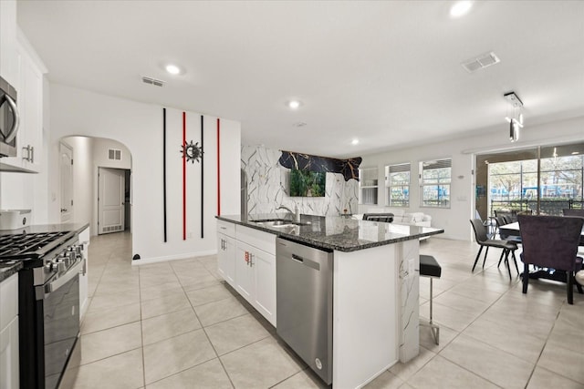 kitchen featuring stainless steel appliances, a breakfast bar, sink, white cabinetry, and dark stone countertops