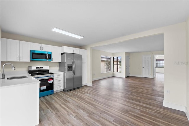 kitchen with light countertops, stainless steel appliances, light wood-style floors, white cabinetry, and a sink