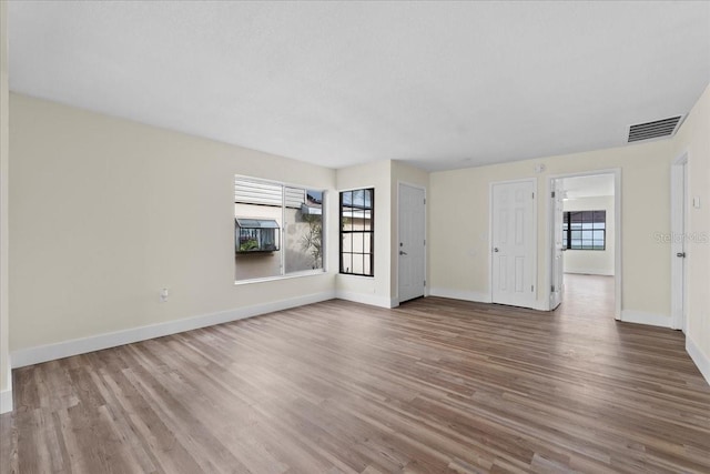 unfurnished living room with wood finished floors, visible vents, and baseboards