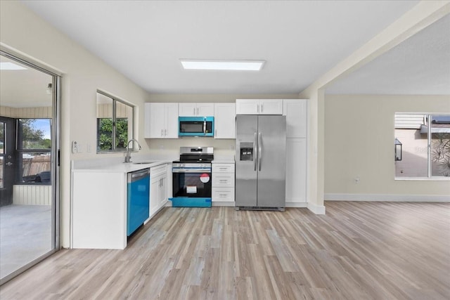 kitchen with light wood finished floors, light countertops, white cabinets, stainless steel appliances, and a sink