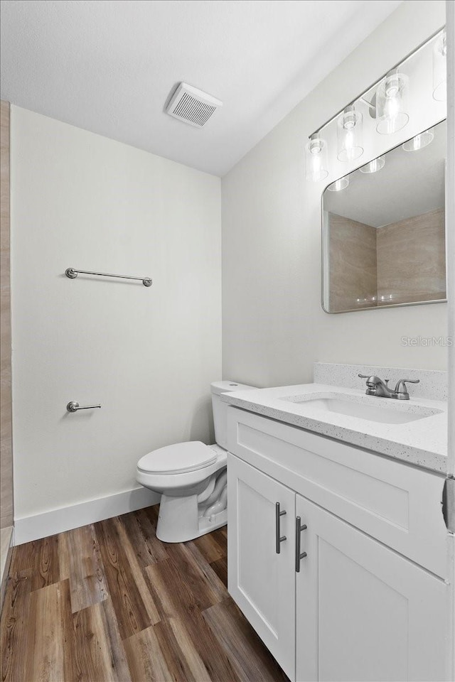 bathroom featuring visible vents, baseboards, toilet, wood finished floors, and vanity