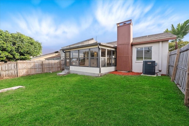 back of house featuring central AC unit, a lawn, a chimney, a fenced backyard, and a sunroom