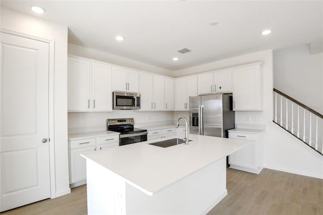 kitchen featuring stainless steel appliances, a kitchen island with sink, white cabinets, and light countertops