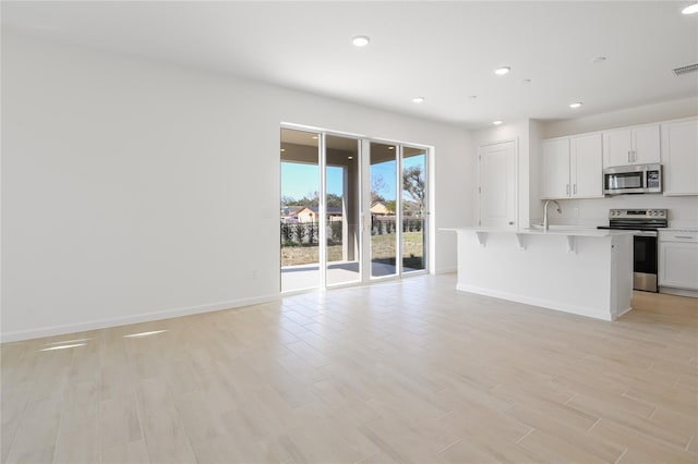 kitchen featuring appliances with stainless steel finishes, open floor plan, a kitchen island with sink, light countertops, and white cabinetry