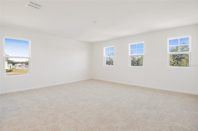 unfurnished room featuring plenty of natural light, visible vents, baseboards, and light colored carpet