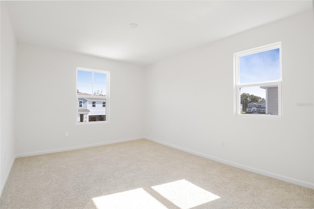 unfurnished room with a healthy amount of sunlight, light carpet, and baseboards