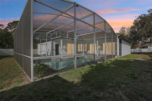back house at dusk with a yard, a fenced in pool, and a lanai