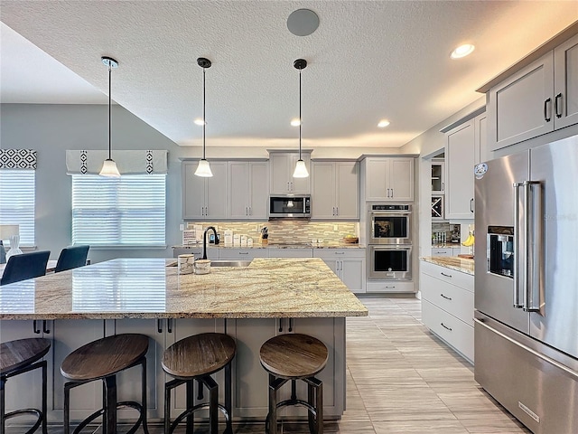 kitchen with light stone counters, a breakfast bar area, stainless steel appliances, a center island with sink, and pendant lighting