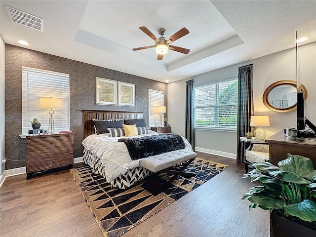 bedroom with baseboards, visible vents, a tray ceiling, and wood finished floors