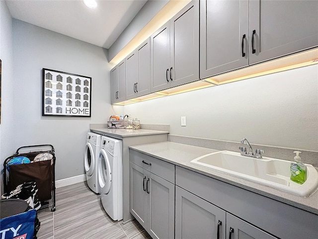 clothes washing area featuring separate washer and dryer, a sink, cabinet space, and baseboards